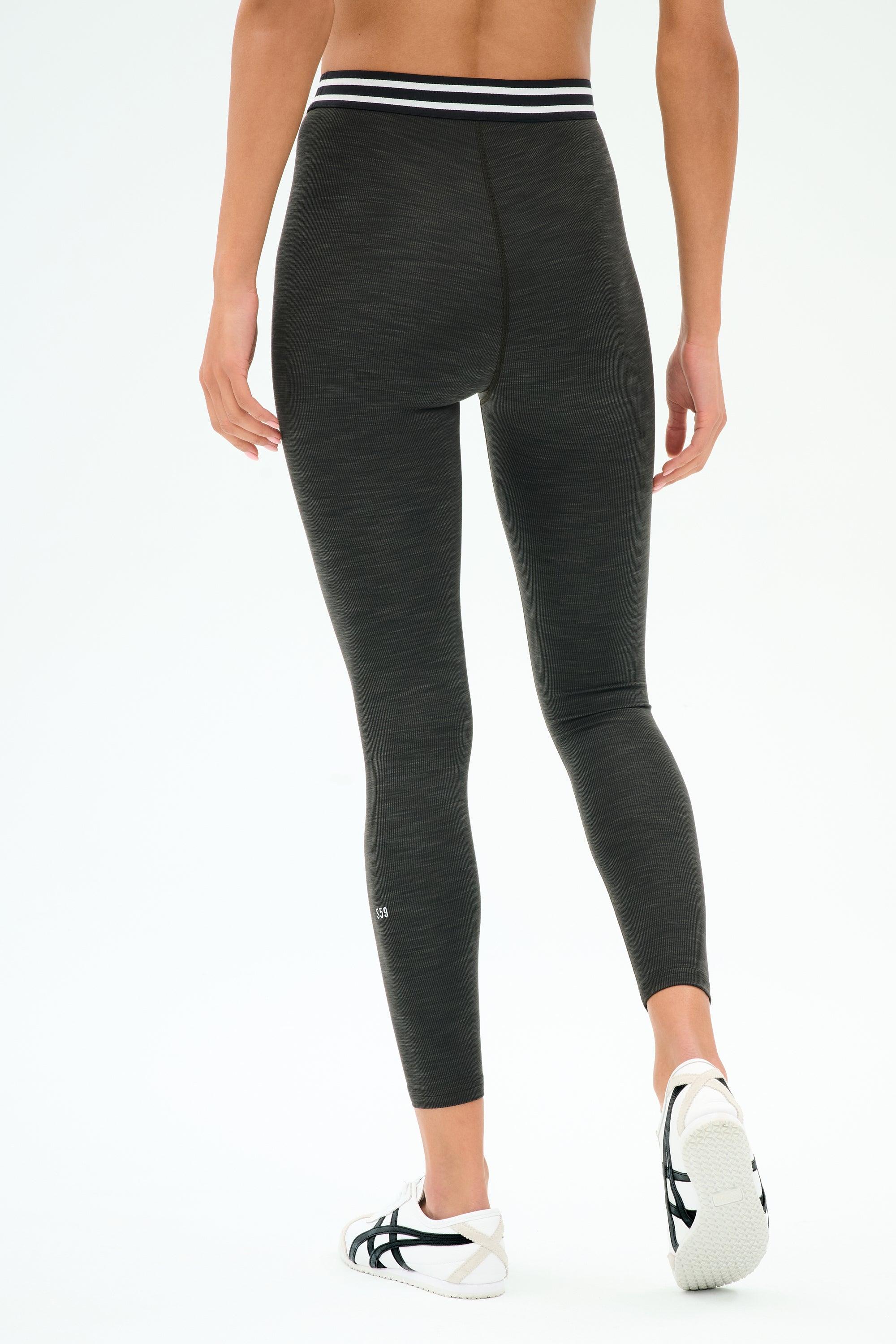 A person wears the SPLITS59 Bailey Active Rib High Waist 7/8 leggings in Heather Graphite, featuring a striped waistband, paired with white athletic shoes against a light background—ideal for gym workouts.