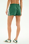 A person wears SPLITS59 Ella Airweight Track Shorts in Arugula/White, featuring stretch fabric and white stripes, paired with white sneakers with green details, standing against a plain background.