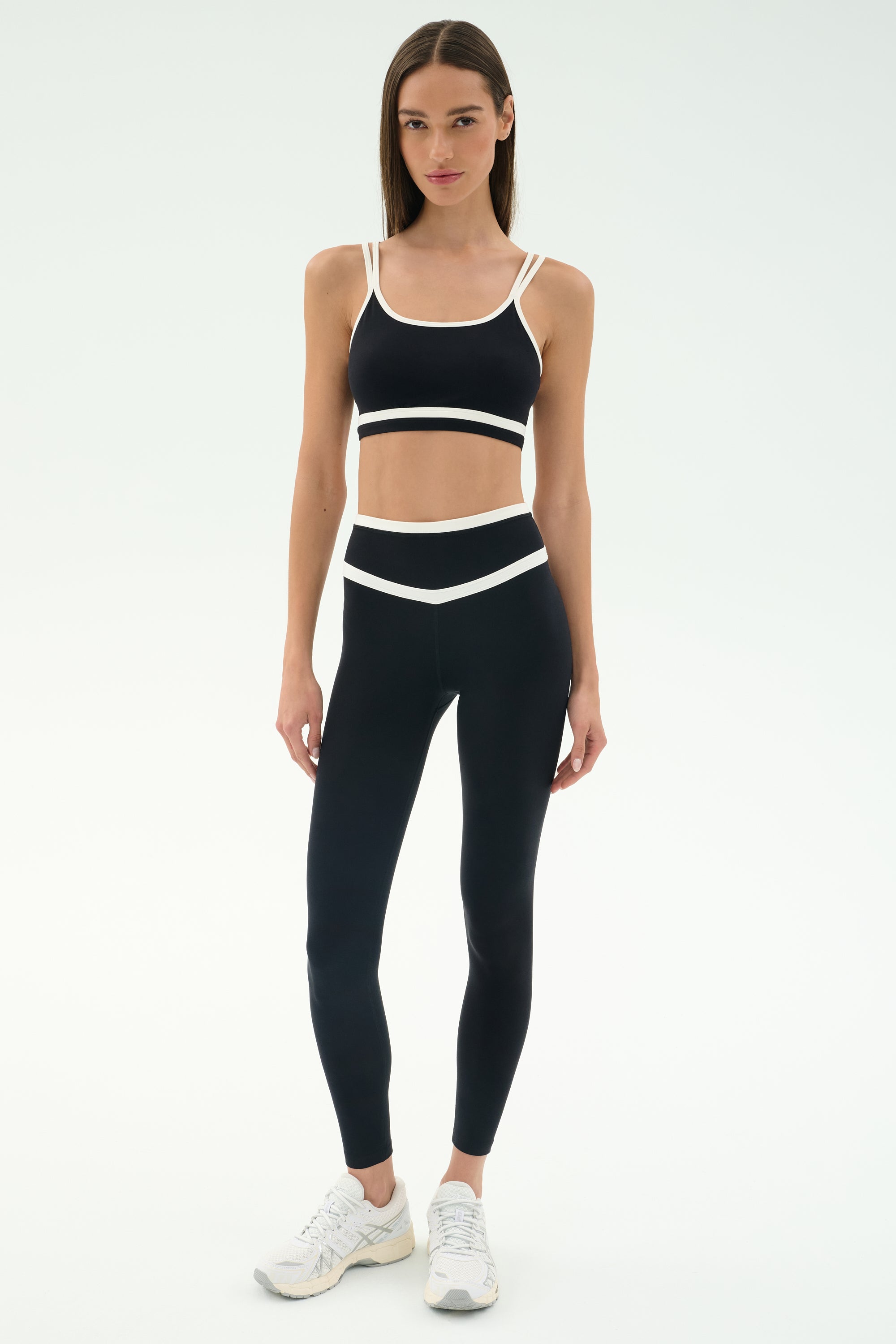 A woman wears the SPLITS59 Mason High Waist Rigor Full Length leggings in Black/White with a matching sports bra and white sneakers, standing against a plain white background.
