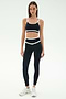 A woman faces forward in the SPLITS59 Eva Rigor Double Strap Bra - Black/White with matching high-waisted leggings and white athletic shoes, ready for gym workouts against a plain light background.