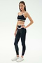 A woman wears the SPLITS59 Mason High Waist Rigor Full Length leggings in Black/White, paired with a black sports bra and white sneakers, standing against a plain light background.