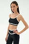 A woman wears the SPLITS59 Eva Rigor Double Strap Bra in Black/White, paired with matching high-waisted leggings, standing with one hand on her hip against a plain white background.