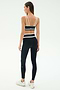 A woman faces away against a plain light background, wearing the SPLITS59 Eva Rigor Double Strap Bra in black/white, paired with matching high-waisted leggings and white sneakers, ready for a gym workout.