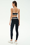 A woman faces away against a plain light background, wearing the SPLITS59 Eva Rigor Double Strap Bra in black/white, paired with matching high-waisted leggings and white sneakers, ready for a gym workout.