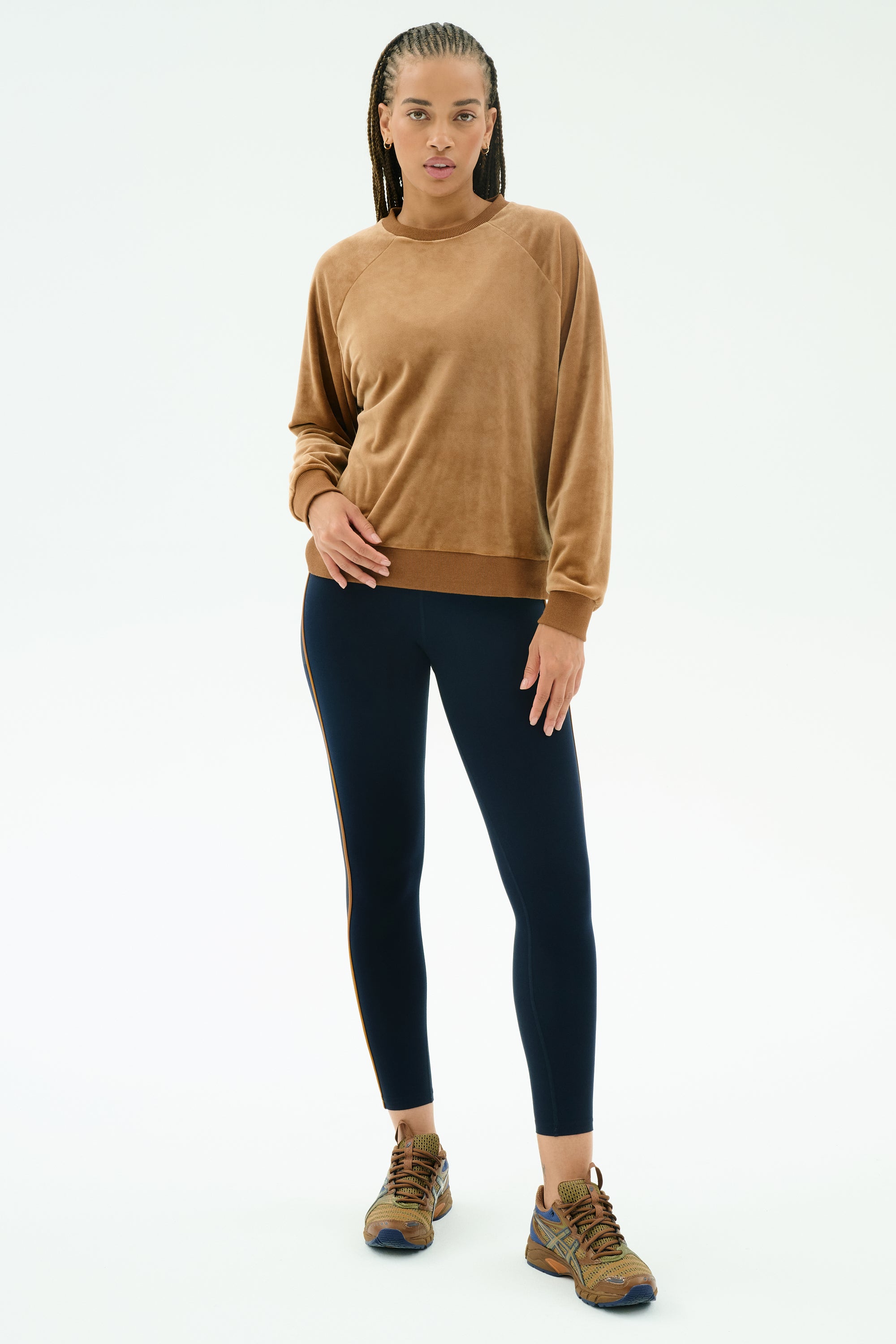 A person wears the SPLITS59 Joy Velour Crewneck in Honey, paired with black leggings and brown sneakers, standing against a plain white background.