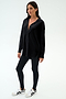A woman stands against a plain background wearing the SPLITS59 Kate Airweight Lite Button Down in black, paired with black leggings and white sneakers with black accents—a versatile layering piece for any outfit.