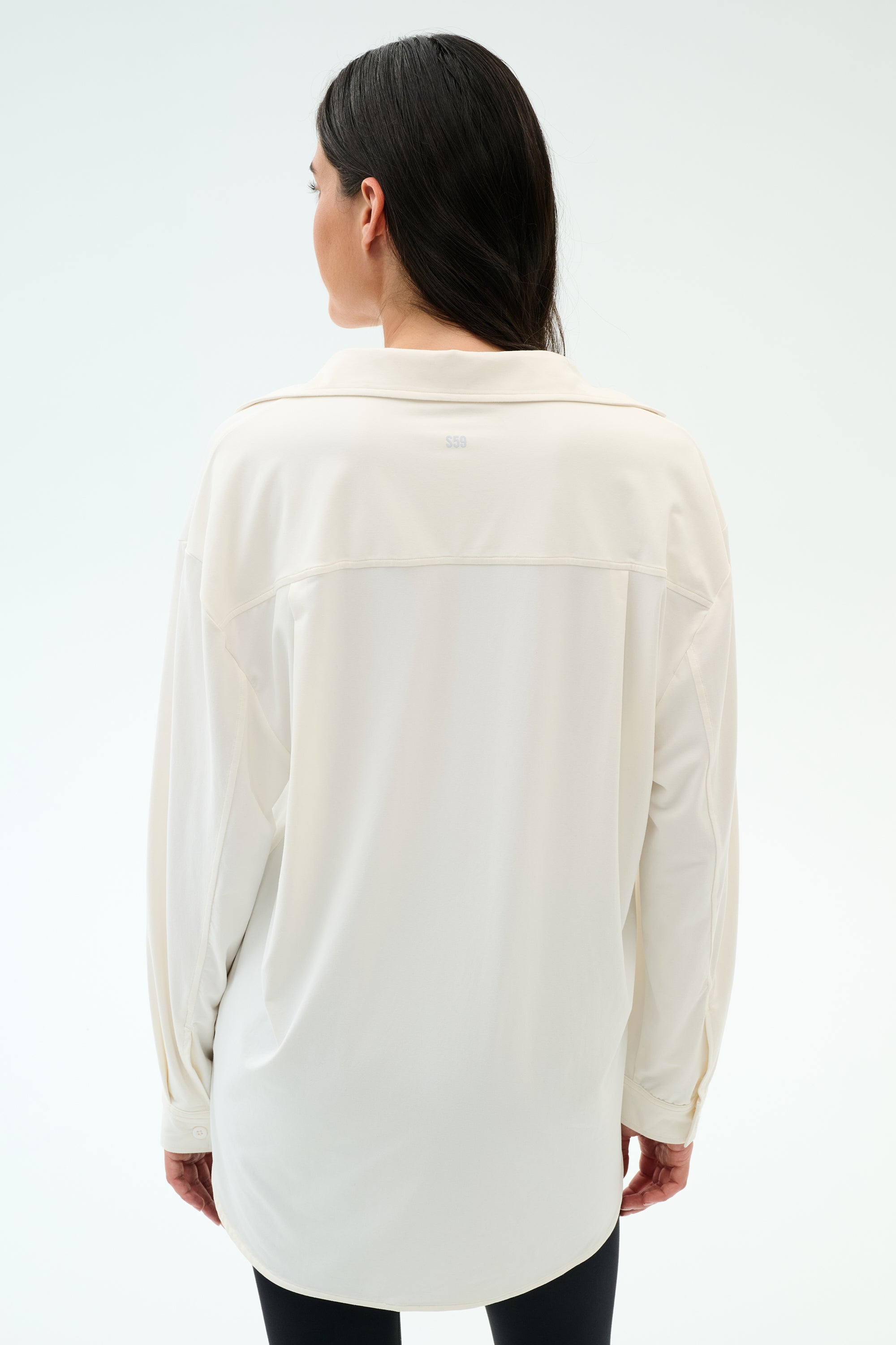 A person with long dark hair wears the SPLITS59 Kate Airweight Lite Button Down in White, facing away from the camera against a plain background—an airy, comfortable layering piece.
