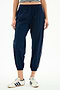 Model wears SPLITS59 Megan Woven Nylon Jogger w/ Piping in Indigo/Creme, featuring a stretchy nylon-spandex blend, paired with white sneakers with blue stripes and a cropped striped top, shown from the waist down against a plain background.
