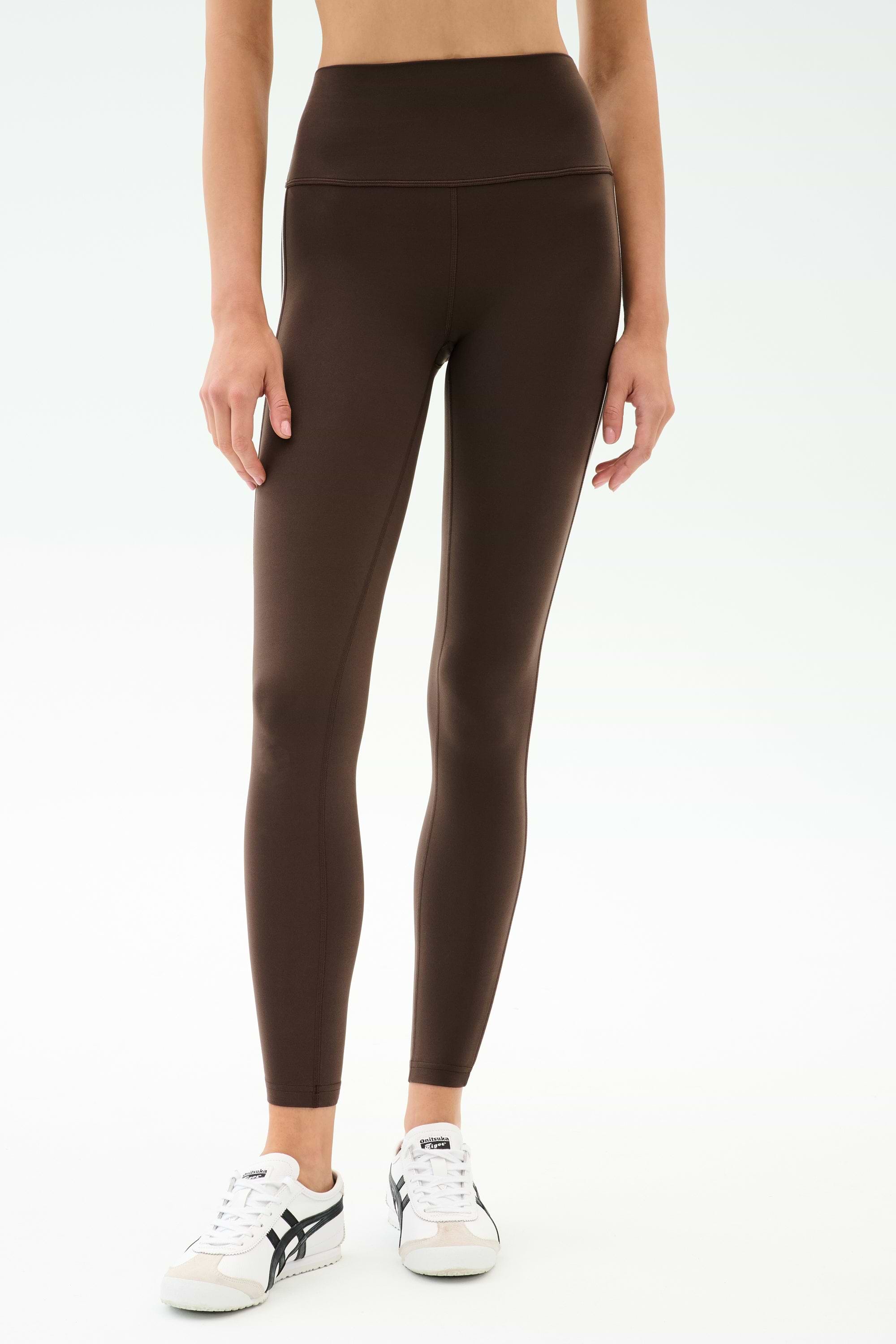 A person wears SPLITS59 Margot Rigor Legging in Dark Chocolate/Black with white sneakers, standing against a plain light background.