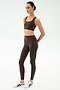 A woman stands against a plain background wearing the SPLITS59 Lexi Rigor Bra in Dark Chocolate/Black, paired with matching high-waisted leggings with white side stripes and white athletic sneakers—ideal for gym workouts.