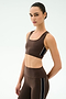 A woman models the SPLITS59 Lexi Rigor Bra in Dark Chocolate/Black, a sports bra-style crop top ideal for gym workouts, paired with matching high-waisted leggings featuring black and white side stripes against a plain light background.