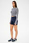 A woman stands against a white background wearing the SPLITS59 Louise Rib Long Sleeve Crop in White/Indigo Stripe, paired with navy bike shorts and matching sneakers—ideal for casual style or gym workouts.