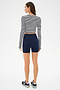 A woman wears the SPLITS59 Louise Rib Long Sleeve Crop in White/Indigo Stripe, paired with navy high-waisted shorts and black sneakers, standing against a white background—ideal for workouts or casual wear.