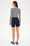 A woman wears the SPLITS59 Louise Rib Long Sleeve Crop in White/Indigo Stripe, paired with navy high-waisted shorts and black sneakers, standing against a white background—ideal for workouts or casual wear.
