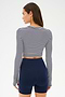 A woman faces away, wearing the SPLITS59 Louise Rib Long Sleeve Crop in White/Indigo Stripe with navy high-waisted athletic shorts against a plain background.