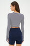 A woman faces away, wearing the SPLITS59 Louise Rib Long Sleeve Crop in White/Indigo Stripe with navy high-waisted athletic shorts against a plain background.
