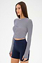 A woman wears the SPLITS59 Louise Rib Long Sleeve Crop in White/Indigo Stripe with high-waisted navy blue biker shorts, standing against a plain white background.