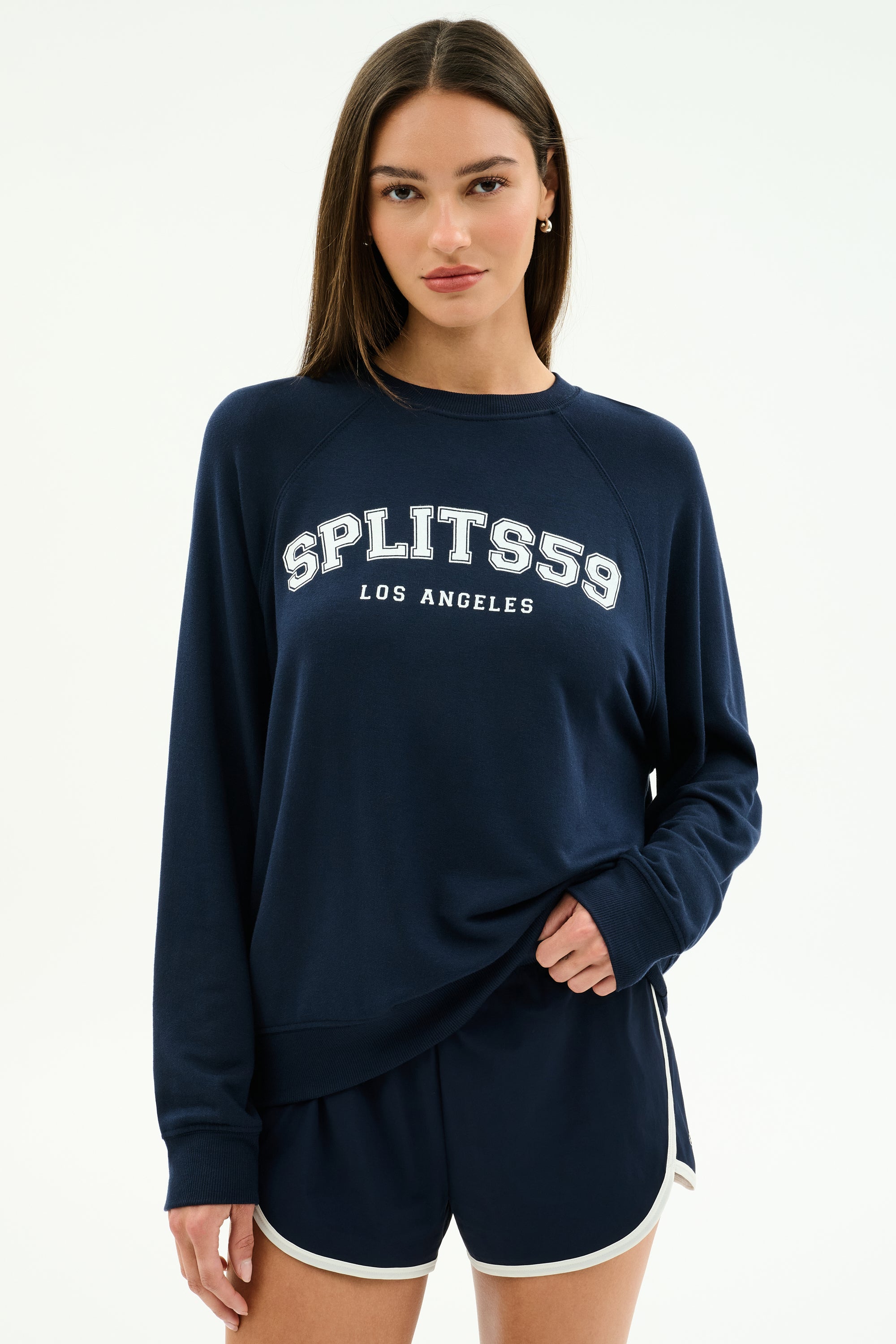 Someone wears the SPLITS59 Andie Oversized Fleece Varsity Graphic Sweatshirt in indigo, featuring "SPLITS59 LOS ANGELES" on the front, paired with matching navy athletic shorts with white trim.