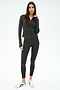 A woman stands in a studio wearing the SPLITS59 Stevie Active Rib Half Zip Waist Length top in Heather Graphite, paired with matching leggings and white sneakers, with a neutral expression.