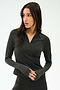 A woman wears the SPLITS59 Stevie Active Rib Half Zip Waist Length top in Heather Graphite, paired with matching pants, standing against a plain light background and looking left with hands clasped.