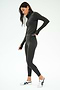 A person in the SPLITS59 Stevie Active Rib Half Zip Waist Length in Heather Graphite stands on a white background, wearing white sneakers and looking down with one hand slightly raised.