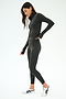 A person in the SPLITS59 Stevie Active Rib Half Zip Waist Length in Heather Graphite stands on a white background, wearing white sneakers and looking down with one hand slightly raised.