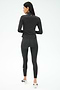 A woman faces away, wearing the SPLITS59 Stevie Active Rib Half Zip Waist Length in Heather Graphite with matching leggings and white athletic shoes, against a plain white background.