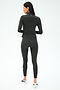 A woman faces away, wearing the SPLITS59 Stevie Active Rib Half Zip Waist Length in Heather Graphite with matching leggings and white athletic shoes, against a plain white background.