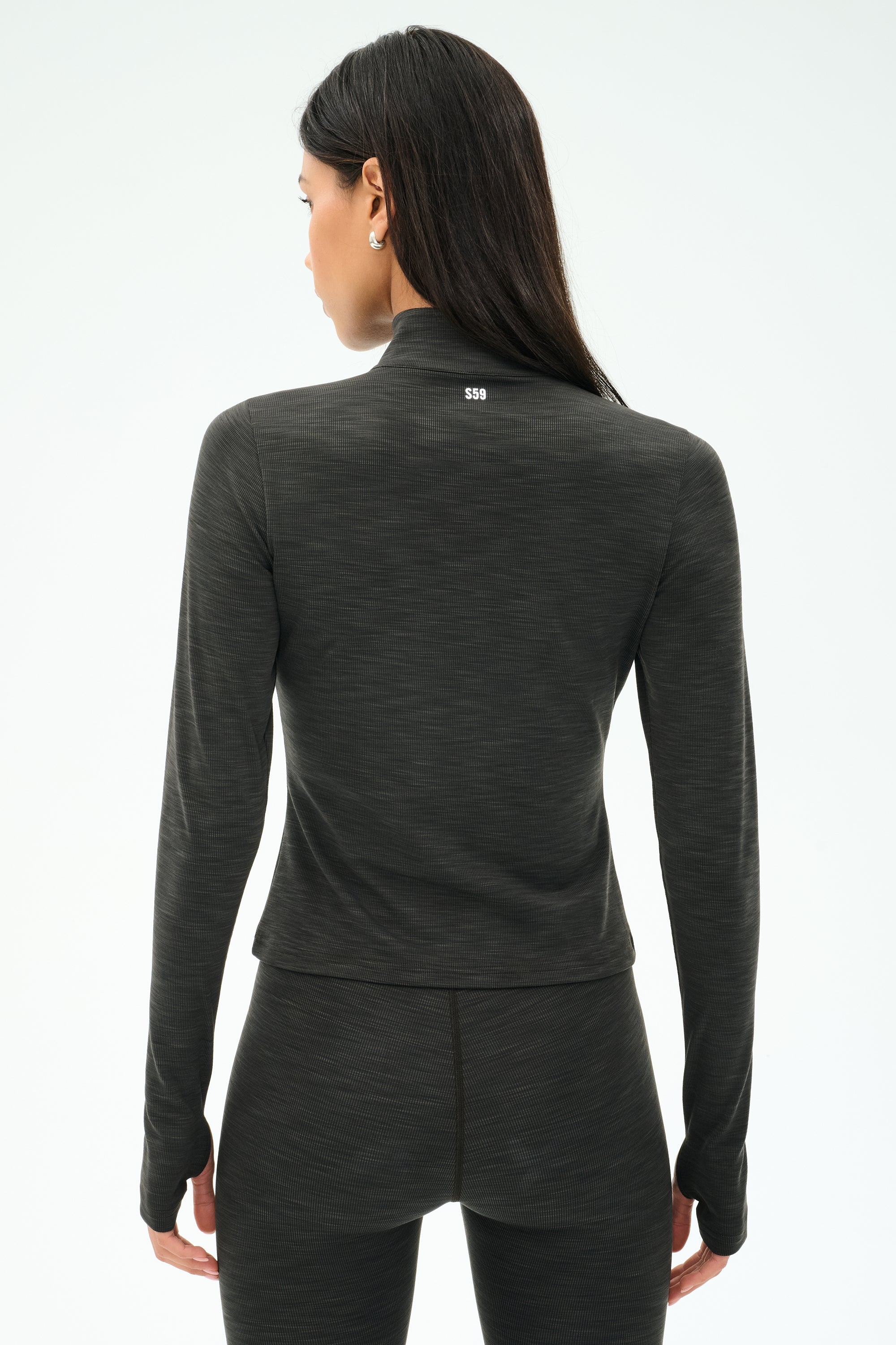 A woman facing away from the camera wears the SPLITS59 Stevie Active Rib Half Zip Waist Length top in Heather Graphite, paired with matching leggings, against a plain background.