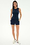 A woman stands facing forward wearing SPLITS59's Ella Airweight Track Short in Indigo/Bright Yellow, paired with a navy spandex sleeveless top and white sneakers with navy stripes.