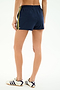 Model wears SPLITS59 Ella Airweight Track Short in Indigo/Bright Yellow, featuring yellow and white side stripes, paired with white Adidas sneakers. Shown from the back against a plain light background.