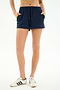Person wearing SPLITS59 Ella Airweight Track Short in Indigo/Bright Yellow and white sneakers, standing with hands in pockets against a plain background.