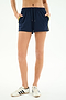 Person wearing SPLITS59 Ella Airweight Track Short in Indigo/Bright Yellow and white sneakers, standing with hands in pockets against a plain background.