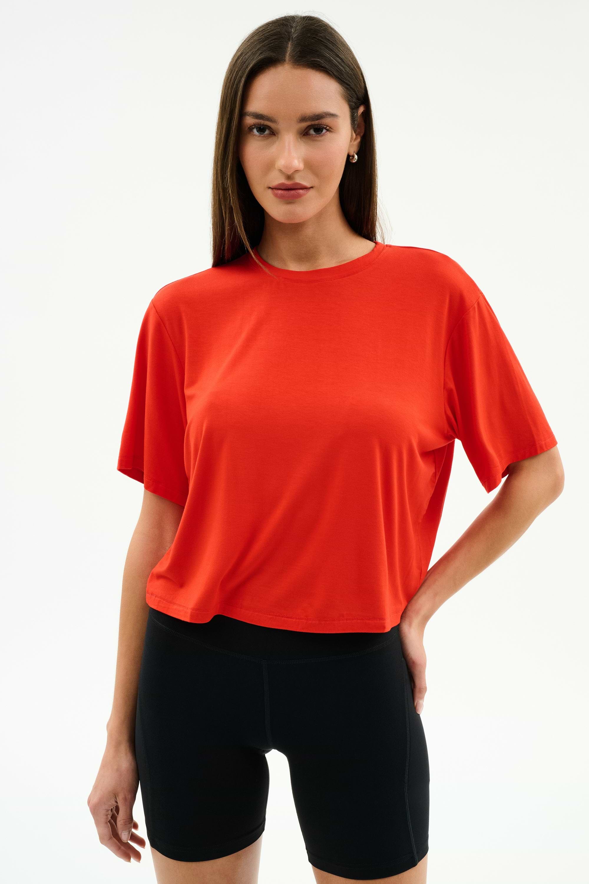 A person models the SPLITS59 Djuna Oversized Jersey Tee in Lotus Red with black shorts against a plain white background, perfect for outdoor or gym workouts.