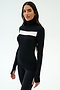 A woman wears the SPLITS59 Lennon Rib Turtleneck in Black/White, featuring a white horizontal chest stripe, standing against a plain light background—perfect for yoga or running.