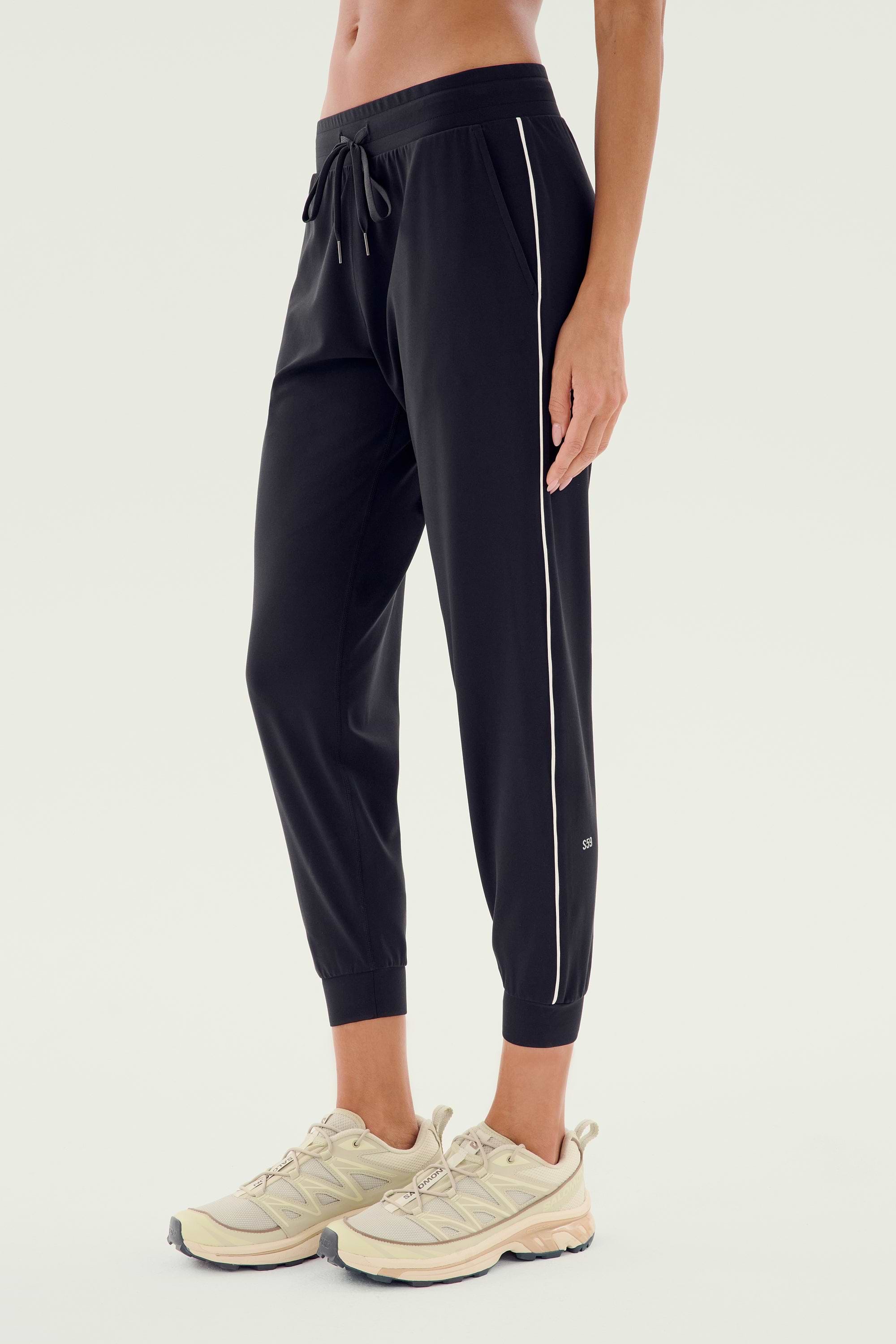 A person sporting the Airweight Jogger 7/8 with Piping in Black/White by SPLITS59, paired with light-colored running shoes, crafted from a comfortable blend of nylon and spandex.