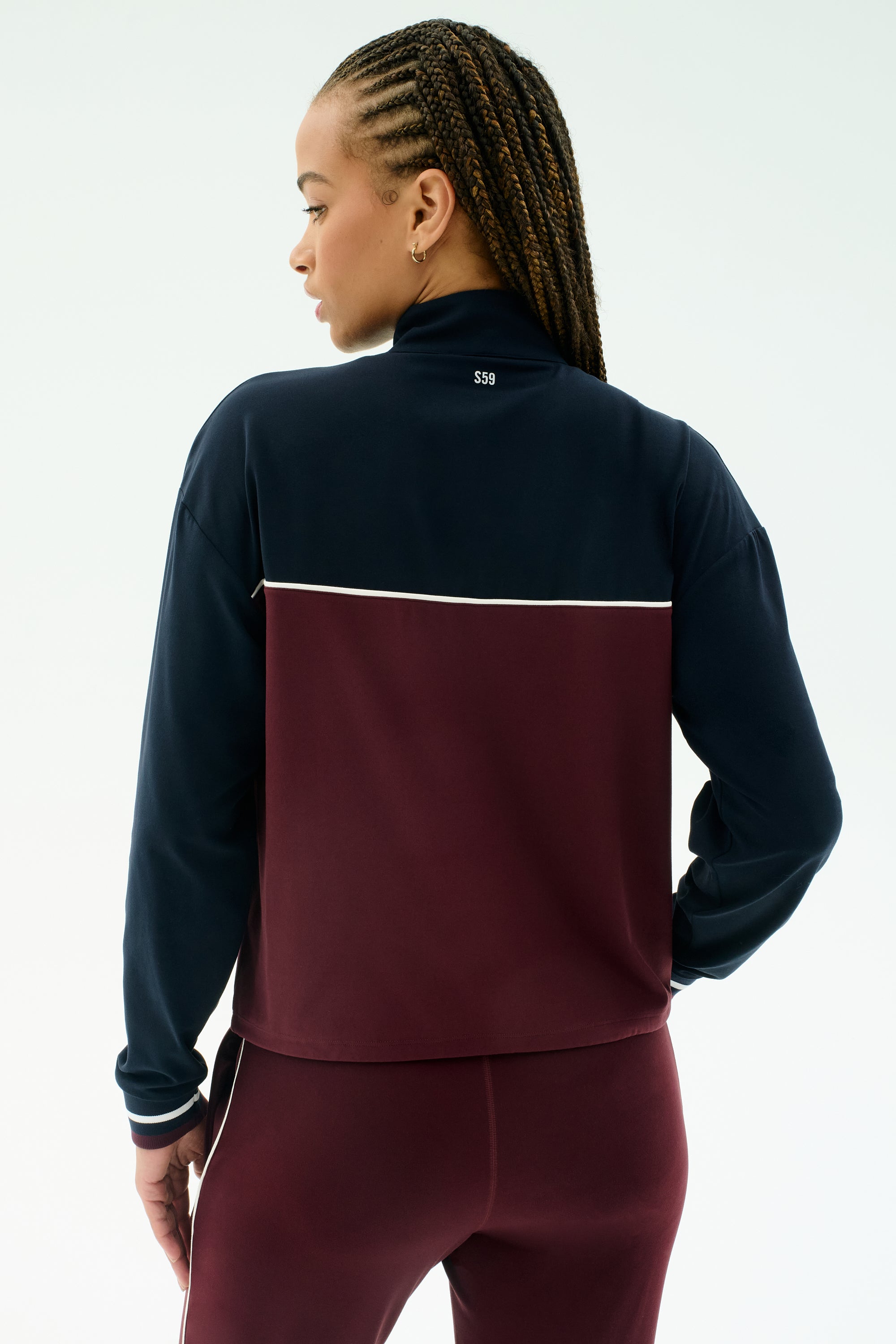 A person with braided hair is shown from the back wearing the SPLITS59 Millie Airweight Half Zip in Dark Cherry/Indigo, standing against a plain light background.