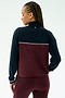 A person with braided hair is shown from the back wearing the SPLITS59 Millie Airweight Half Zip in Dark Cherry/Indigo, standing against a plain light background.