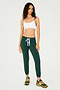 Full front view of woman with dark wavy hair wearing dark green sweatpant jogger with white drawstring and white bra with spaghetti straps paired with dark green, orange and light green shoes