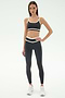 A woman faces forward wearing the SPLITS59 Eva Rigor Double Strap Bra in Graphite/White with matching leggings and white sneakers, great for gym workouts, against a plain light background.