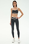 A woman faces forward wearing the SPLITS59 Eva Rigor Double Strap Bra in Graphite/White with matching leggings and white sneakers, great for gym workouts, against a plain light background.