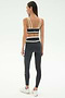 A woman faces away in the SPLITS59 Eva Rigor Double Strap Bra in Graphite/White, paired with high-waisted leggings and white sneakers—an ideal gym-ready look—against a plain white background.