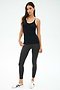 A woman stands against a plain background wearing the SPLITS59 Ashby Rib Tank in Black/White—ideal for yoga or gym workouts—paired with dark gray leggings and white sneakers.