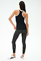 A woman faces away, wearing the SPLITS59 Ashby Rib Tank in Black/White, paired with dark gray leggings and white sneakers—ideal activewear for gym sessions against a plain background.