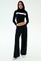 A woman stands facing forward against a plain background wearing SPLITS59's Brynn Airweight Pant in black, paired with a black nylon long-sleeve turtleneck featuring a white horizontal stripe and white shoes.