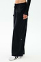 A person wears SPLITS59 Brynn Airweight Pant in black, styled with white sneakers featuring black stripes and a long-sleeve black top, standing against a plain light background.
