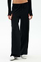 Wearing SPLITS59's Brynn Airweight Pant in Black with a black long-sleeve top and white sneakers, the person stands against a plain white background.