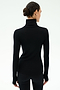 A person with dark hair in a low bun wears the SPLITS59 Jackson Rib Full Length Turtleneck - Black/White and black pants, standing against a plain light background, facing away from the camera.