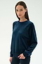 A woman stands against a plain light background wearing the SPLITS59 Joy Velour Crewneck in Indigo and black pants.