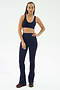 A person faces forward, wearing the SPLITS59 Raquel High Waist Flared Legging in Indigo/Dark Cherry and a navy sports bra, paired with burgundy sneakers against a plain white background.